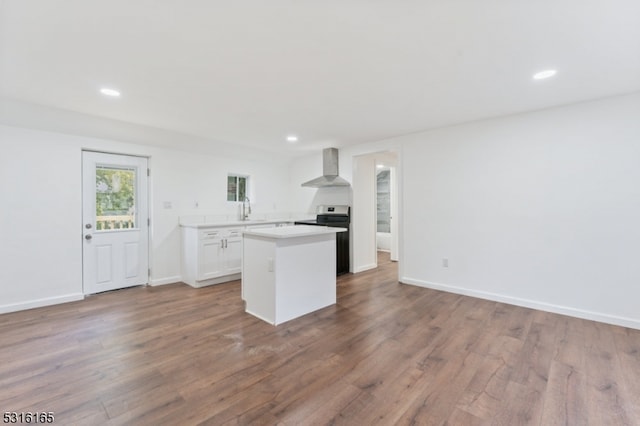 kitchen with sink, white cabinetry, wall chimney range hood, and hardwood / wood-style flooring