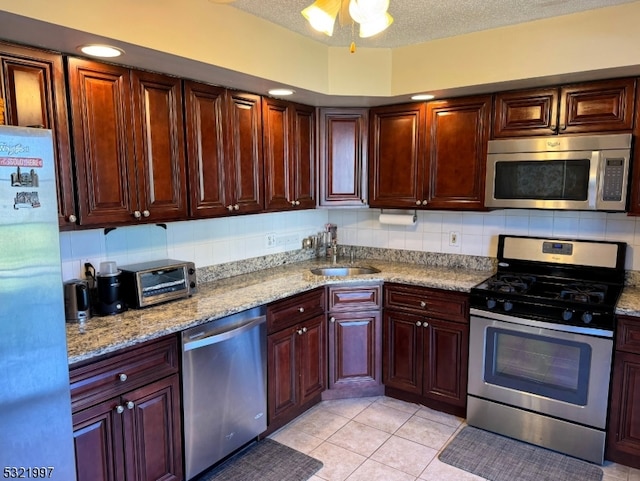 kitchen featuring light stone counters, decorative backsplash, a textured ceiling, light tile patterned floors, and appliances with stainless steel finishes