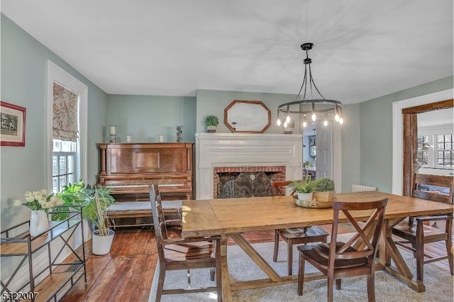 dining room with a healthy amount of sunlight, wood-type flooring, and a brick fireplace