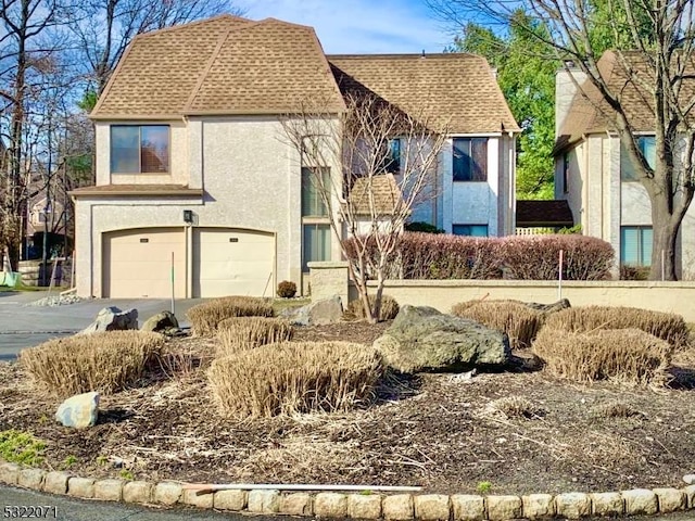 tudor-style house with stucco siding, an attached garage, concrete driveway, and a shingled roof