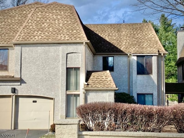 view of front facade with stucco siding, driveway, an attached garage, and a shingled roof