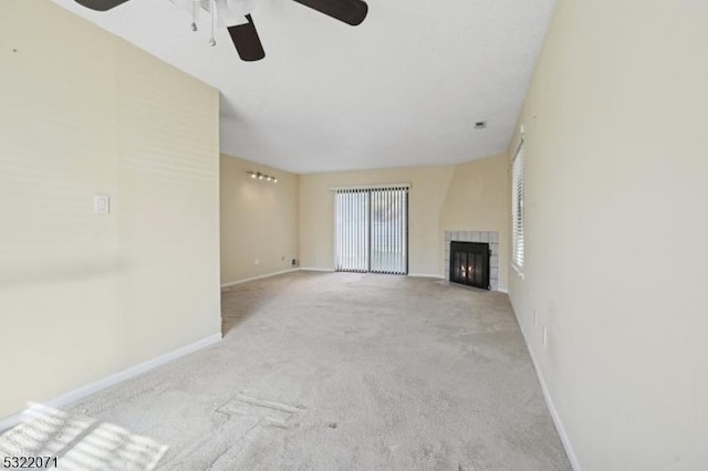 unfurnished living room featuring a tiled fireplace, ceiling fan, baseboards, and carpet