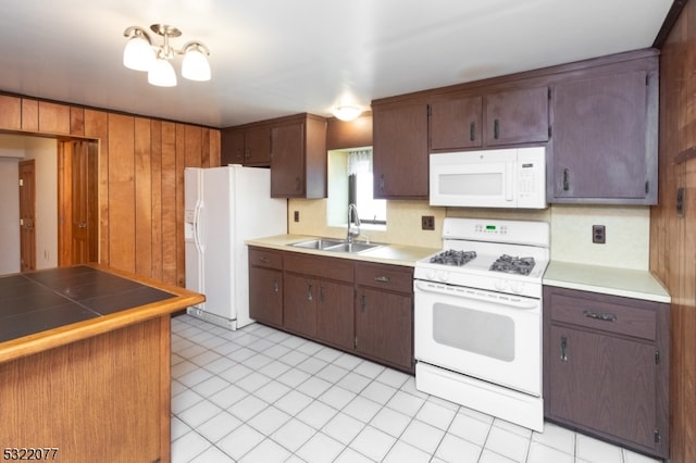 kitchen featuring a chandelier, wooden walls, sink, dark brown cabinets, and white appliances