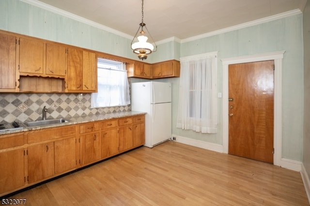 kitchen with hanging light fixtures, sink, ornamental molding, white fridge, and light hardwood / wood-style flooring