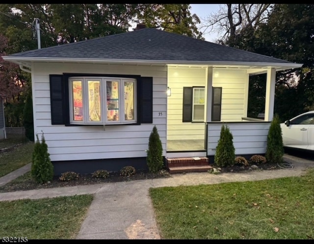 bungalow-style house featuring a porch, roof with shingles, and a front yard