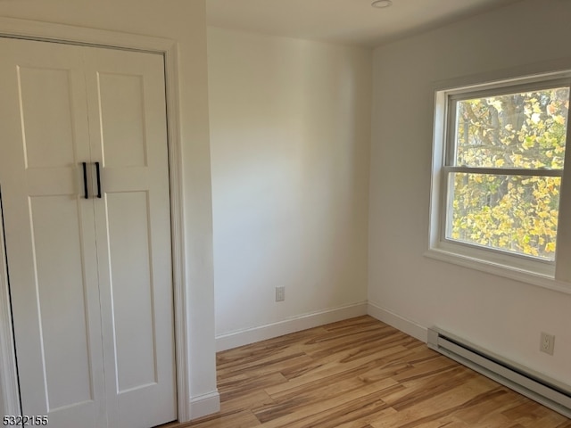 unfurnished bedroom featuring baseboards, a baseboard radiator, and light wood-style floors