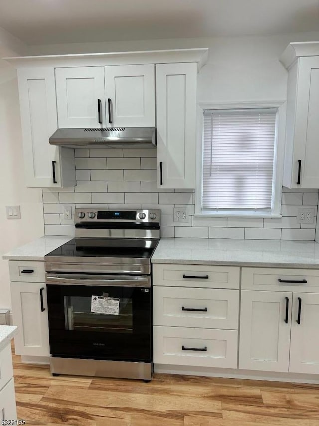 kitchen with under cabinet range hood, white cabinetry, light wood-style floors, stainless steel electric range, and tasteful backsplash