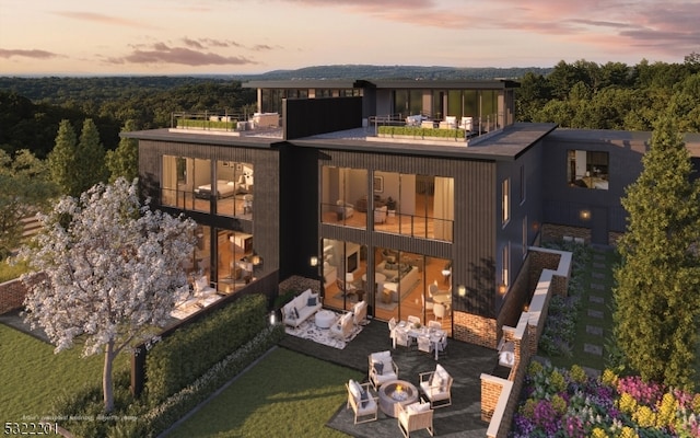 back house at dusk with an outdoor living space, a balcony, a patio area, and a lawn