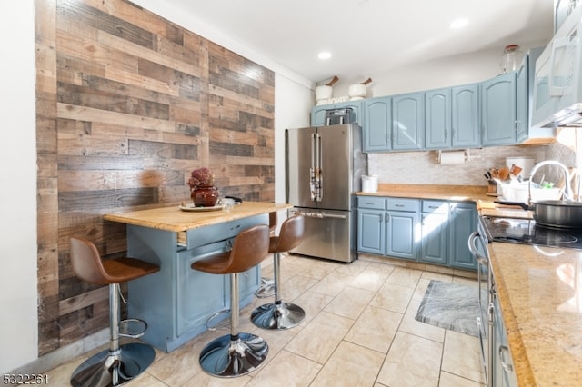 kitchen with a kitchen breakfast bar, wooden walls, blue cabinetry, appliances with stainless steel finishes, and light stone counters