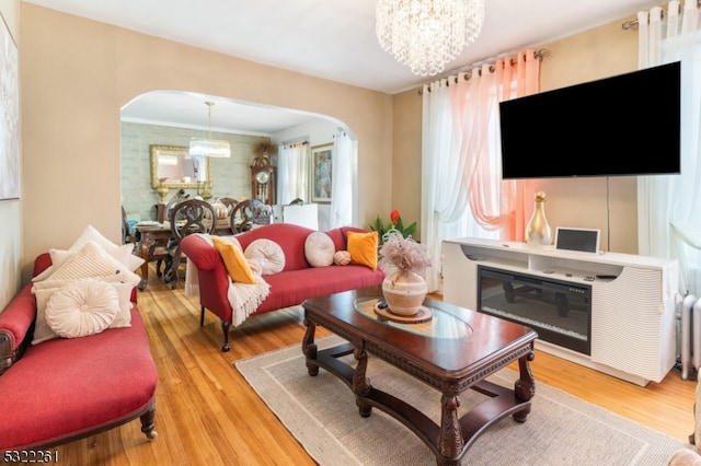 living room with an inviting chandelier, ornamental molding, and light wood-type flooring