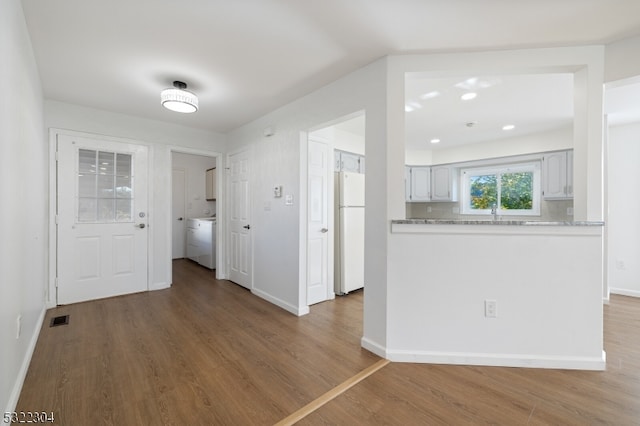 kitchen with white refrigerator, hardwood / wood-style flooring, tasteful backsplash, washer / dryer, and kitchen peninsula