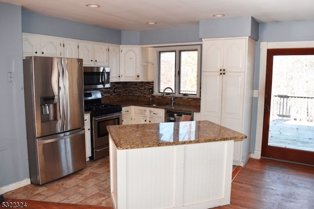 kitchen featuring stainless steel appliances, dark stone counters, white cabinetry, sink, and a center island