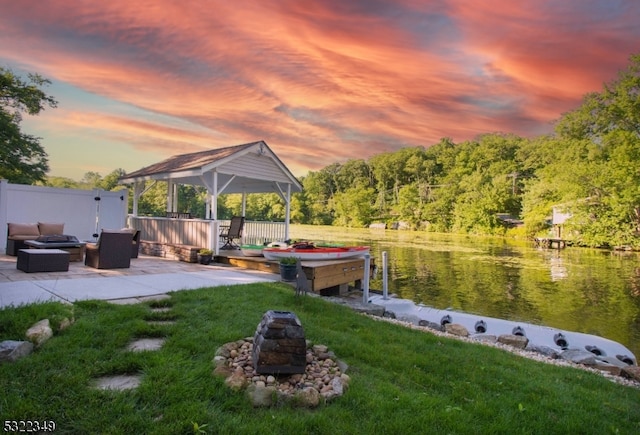 dock area with a gazebo, a water view, a patio, an outdoor fire pit, and a lawn