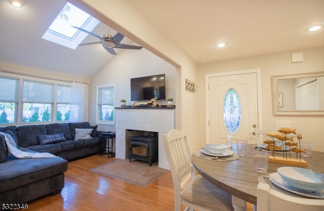 living room featuring vaulted ceiling, wood-type flooring, a wood stove, and ceiling fan