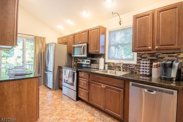 kitchen with lofted ceiling, backsplash, dark stone countertops, sink, and appliances with stainless steel finishes