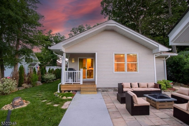 back house at dusk featuring a yard, an outdoor living space with a fire pit, and a patio area