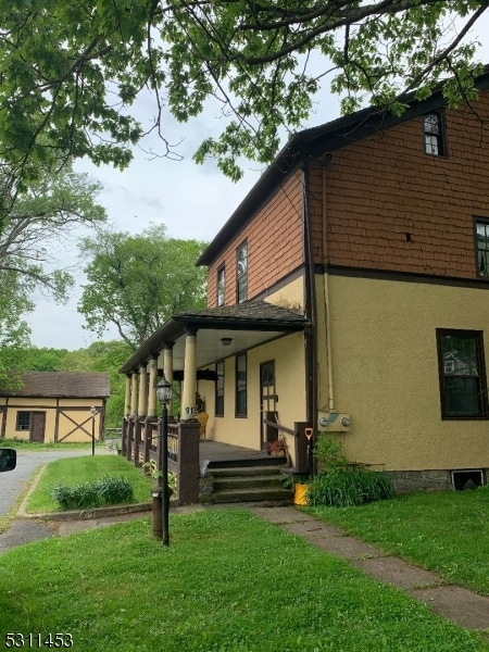 view of property exterior with a lawn, an outbuilding, and a porch