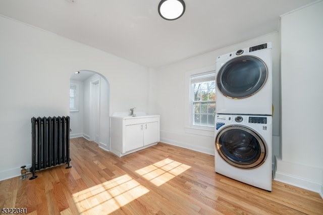 laundry room with radiator heating unit, stacked washer / dryer, and light hardwood / wood-style flooring