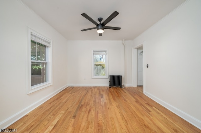 empty room featuring a wealth of natural light, ceiling fan, light wood-type flooring, and radiator