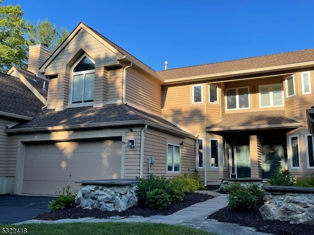 view of front facade with driveway, an attached garage, and a shingled roof