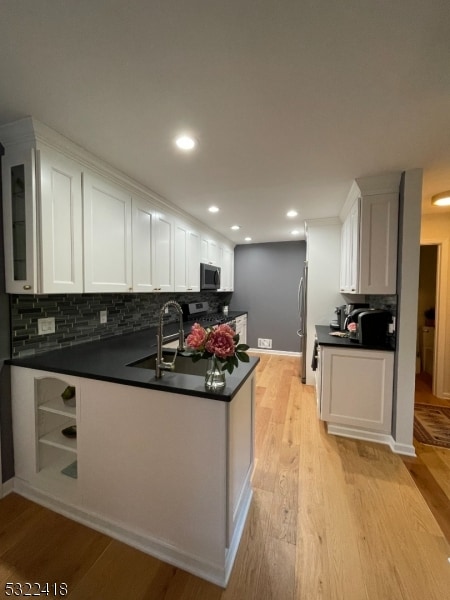 kitchen featuring sink, kitchen peninsula, appliances with stainless steel finishes, white cabinets, and light wood-type flooring