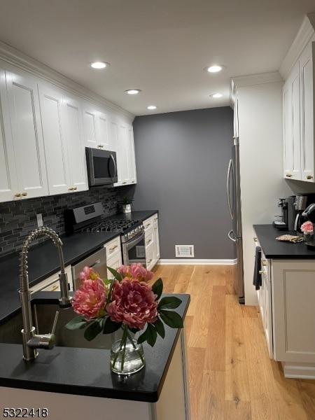 kitchen featuring decorative backsplash, appliances with stainless steel finishes, ornamental molding, white cabinets, and light hardwood / wood-style floors