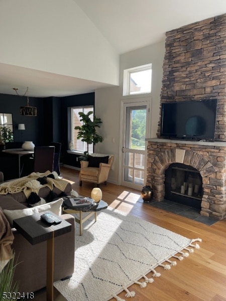 living room with a stone fireplace, high vaulted ceiling, and wood-type flooring