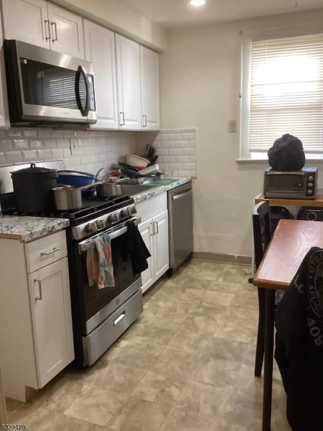 kitchen featuring backsplash, white cabinetry, light stone countertops, and stainless steel appliances