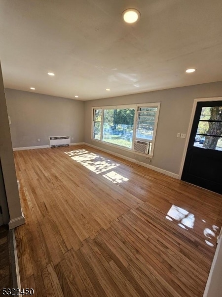 unfurnished living room with hardwood / wood-style floors, cooling unit, and radiator heating unit