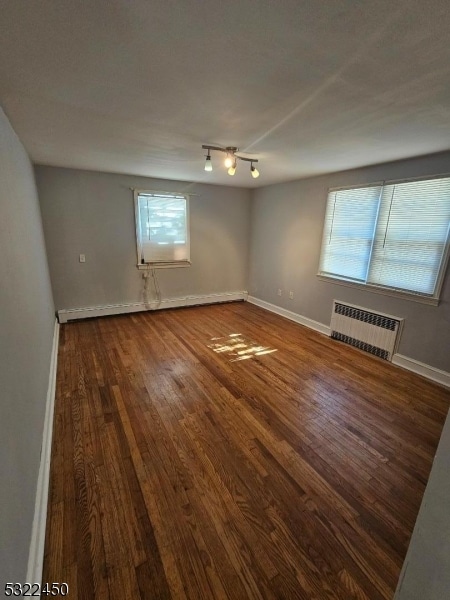 spare room with hardwood / wood-style flooring, a healthy amount of sunlight, and radiator heating unit