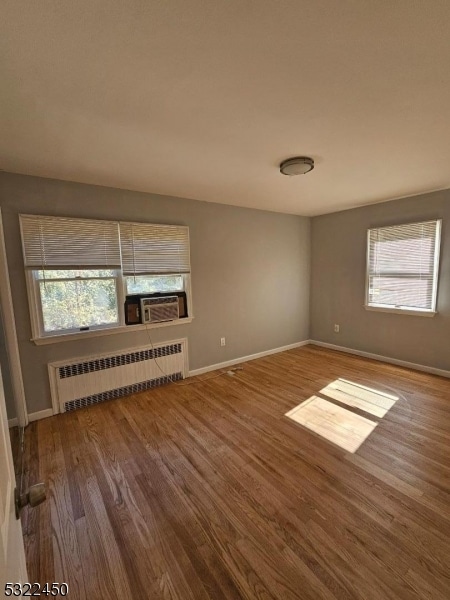 unfurnished room featuring a wealth of natural light, cooling unit, wood-type flooring, and radiator