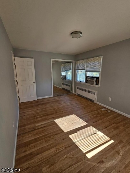 unfurnished living room featuring cooling unit, radiator heating unit, and dark hardwood / wood-style floors