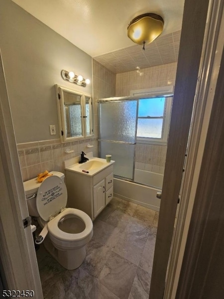 full bathroom with toilet, combined bath / shower with glass door, vanity, and tile walls