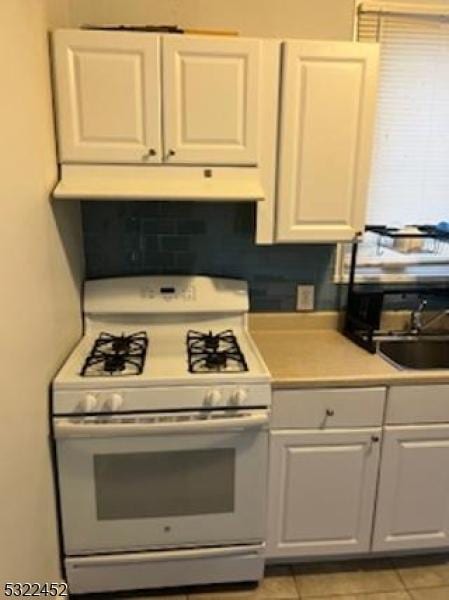 kitchen featuring light tile patterned flooring, white cabinetry, gas range gas stove, and sink