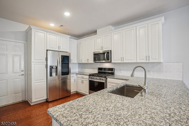 kitchen with white cabinets, appliances with stainless steel finishes, sink, and light stone counters