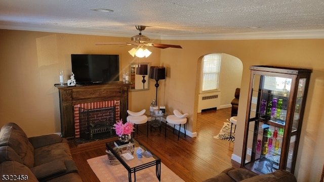 living room featuring a brick fireplace, radiator, hardwood / wood-style floors, a textured ceiling, and ceiling fan