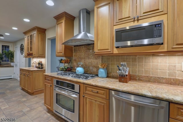 kitchen featuring wall chimney range hood, sink, stainless steel appliances, light stone counters, and decorative backsplash