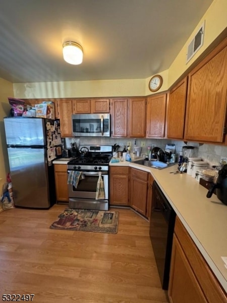 kitchen with stainless steel appliances, light hardwood / wood-style floors, sink, and tasteful backsplash