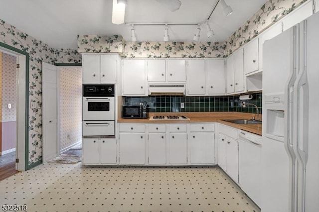 kitchen featuring white appliances, wallpapered walls, light floors, under cabinet range hood, and a sink