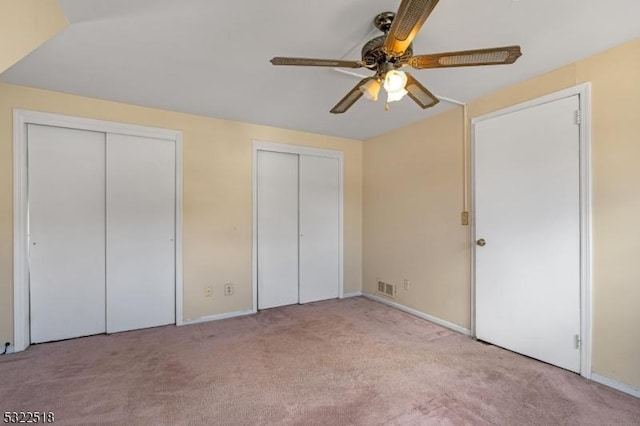 unfurnished bedroom with carpet floors, a ceiling fan, visible vents, and two closets