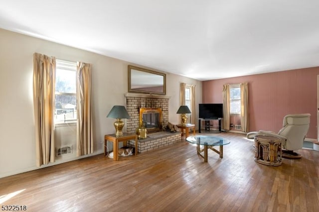 living area featuring plenty of natural light, a brick fireplace, and wood finished floors