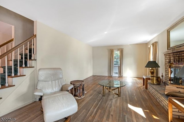 sitting room featuring stairway, a brick fireplace, and wood finished floors