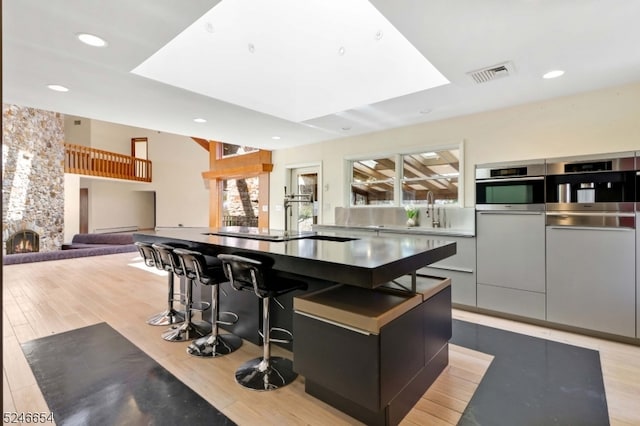 kitchen featuring a fireplace, a spacious island, stainless steel oven, a kitchen breakfast bar, and light hardwood / wood-style floors