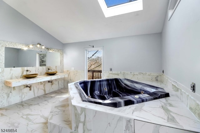 bathroom with vanity, vaulted ceiling with skylight, and tiled tub