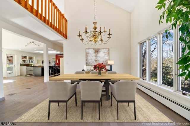 dining space featuring baseboard heating, a chandelier, light hardwood / wood-style flooring, and high vaulted ceiling