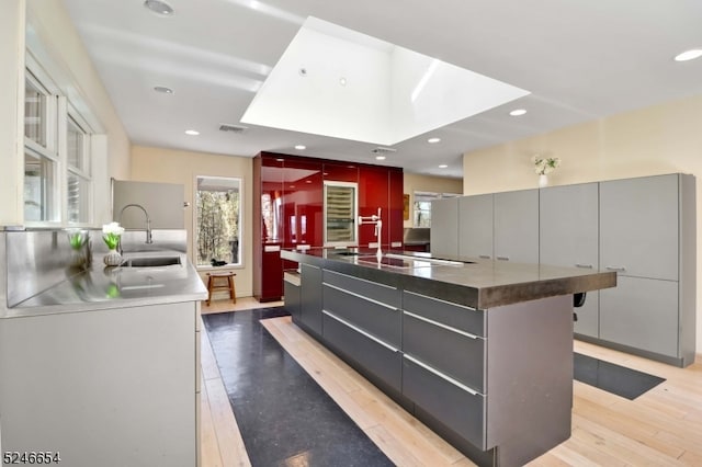 kitchen featuring a breakfast bar area, a spacious island, light wood-type flooring, a skylight, and sink