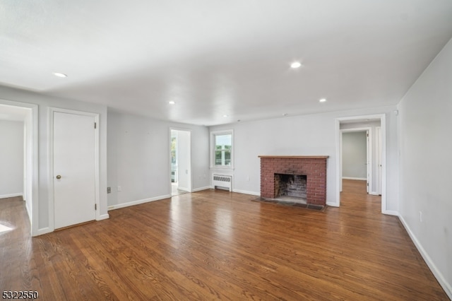 unfurnished living room with radiator, hardwood / wood-style flooring, and a brick fireplace