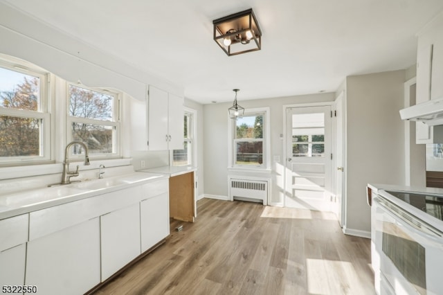 kitchen with a wealth of natural light, radiator, hanging light fixtures, and white cabinets