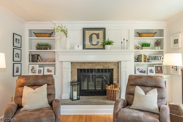 living area with built in features, hardwood / wood-style flooring, crown molding, and a fireplace