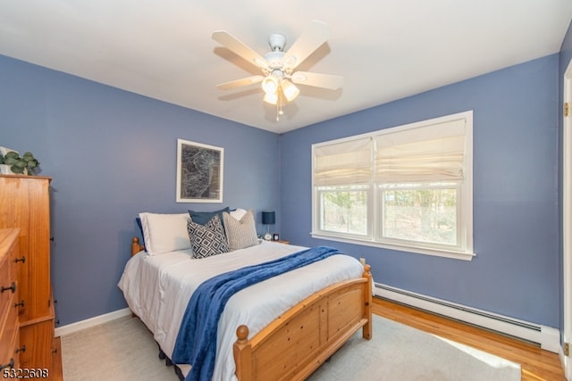 bedroom with light hardwood / wood-style floors, ceiling fan, and a baseboard heating unit